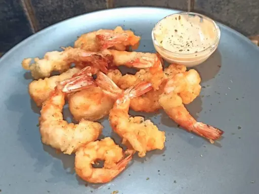 Gamberi in tempura dorati e croccanti, serviti su un piatto blu con una ciotolina di salsa cremosa.