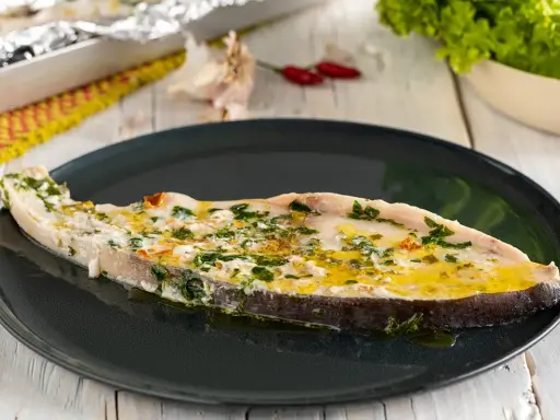 Un succulento pesce spada al forno, condito con erbe aromatiche e olio d'oliva, servito su un piatto scuro.