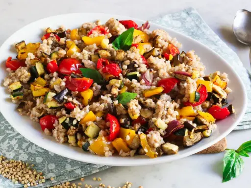 Un piatto colorato di insalata di grano saraceno con verdure miste arrosto: peperoni, zucchine, melanzane e pomodorini.