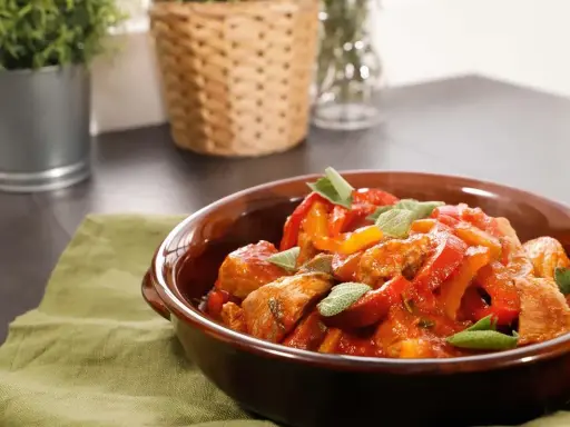 Un saporito spezzatino di vitello con peperoni rossi e gialli, guarnito con foglie di salvia fresca, servito in una ciotola di terracotta.