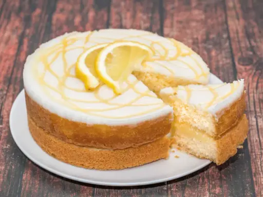 Torta al limone soffice e profumata, con glassa bianca e decorazioni gialle, guarnita con fette di limone.