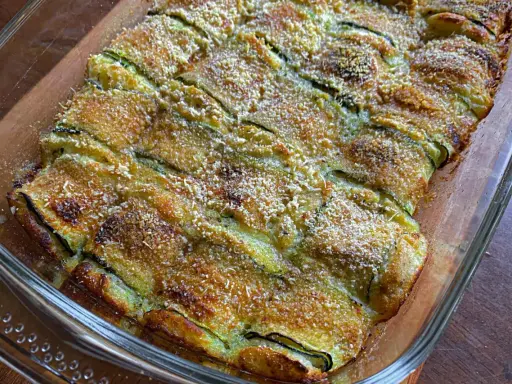 Involtini di zucchine grigliate al forno, dorati e croccanti, in una pirofila di vetro.