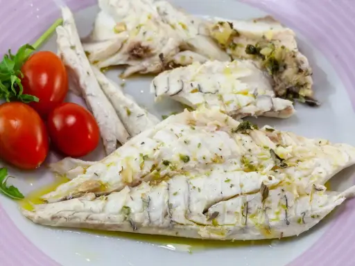 Filetti di branzino in padella, conditi con erbe aromatiche e olio d'oliva, serviti con pomodorini e rucola.