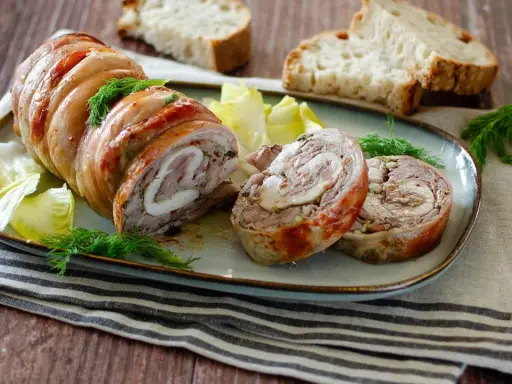 Coniglio in porchetta, un rotolo di carne succulento con erbe aromatiche, servito con pane tostato e insalata.