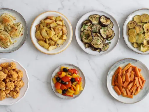 Sette piatti di verdure in friggitrice ad aria: finocchi, patate, melanzane, zucchine, cavolfiore, peperoni e carote.