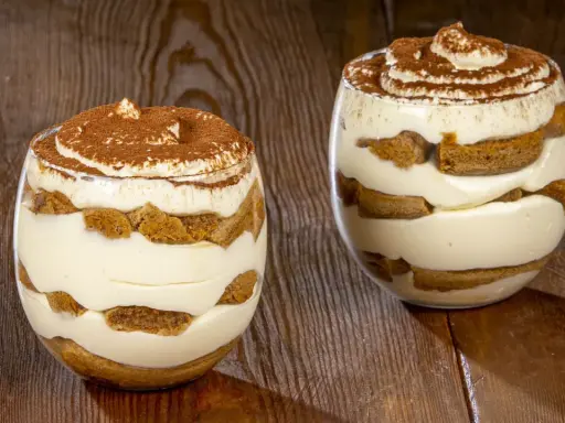 Due bicchieri di delizioso tiramisù senza uova, con strati di crema e savoiardi, spolverati di cacao.