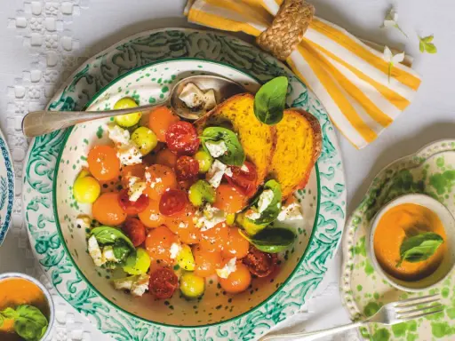 Deliziosa insalata con melone, pomodorini, formaggio e basilico, servita con pane tostato e una ciotolina di gazpacho.