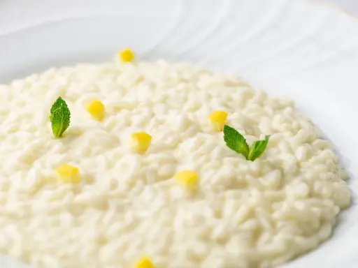 Un cremoso risotto al limone, guarnito con cubetti di limone e foglie di menta fresca, su un piatto bianco.