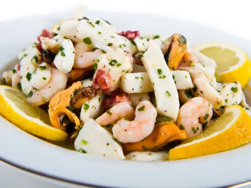 Deliziosa insalata di mare con verdure, gamberi, calamari, polpo e cozze, guarnita con spicchi di limone fresco e prezzemolo tritato.