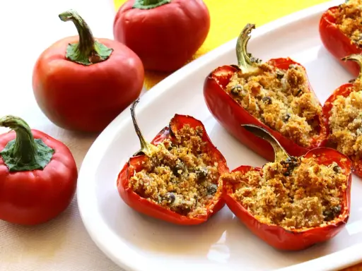Peperoni ripieni di tonno e pangrattato, dorati e invitanti, su un piatto bianco.