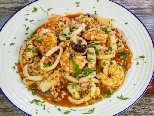 Un invitante risotto alla pescatora, ricco di gamberi, calamari e cozze, guarnito con prezzemolo fresco.