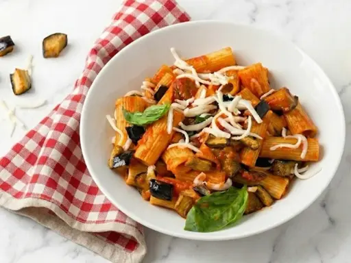 Piatto di pasta alla norma con melanzane fritte, pomodoro, basilico e ricotta salata grattugiata.