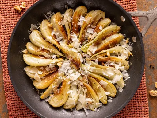 Finocchi in padella dorati, guarniti con scaglie di formaggio e noci croccanti. Un contorno saporito e invitante.