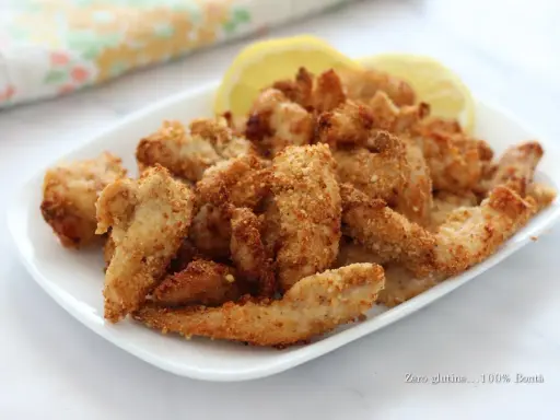 Straccetti di pollo in friggitrice ad aria, dorati e croccanti, serviti con spicchi di limone.