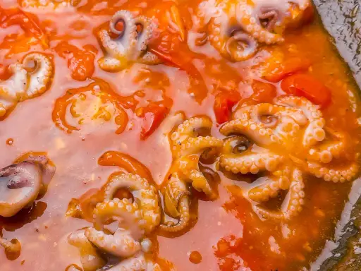 Piccolo polpo alla luciana in un sugo rosso ricco, con tentacoli visibili e pomodorini.