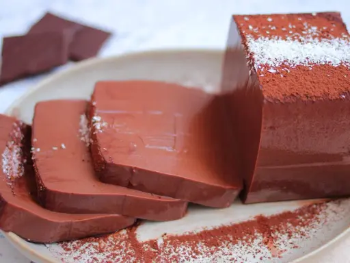 Fette di budino al cioccolato, spolverate di cacao e cocco, su un piatto.