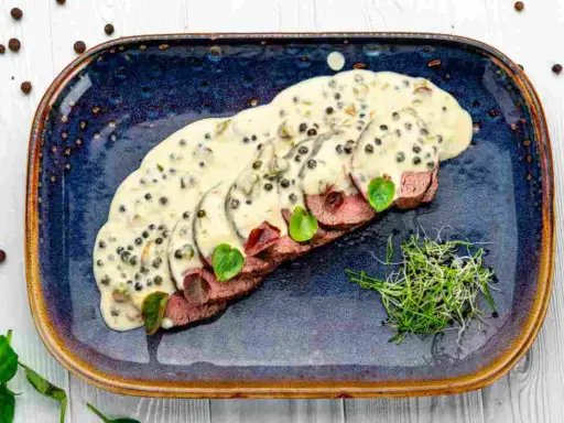 Fette affettate in salsa cremosa al pepe verde, guarnite con germogli freschi. Un delizioso filetto al pepe verde pronto da gustare.