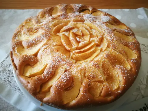 Deliziosa torta di mele senza glutine, decorata con fettine di mela disposte a rosa al centro e petali tutt'intorno, spolverata di zucchero a velo.