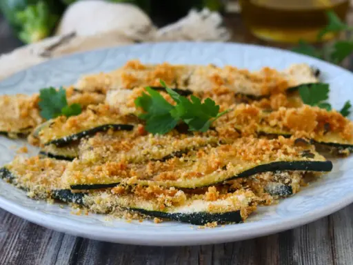 Fette di zucchine al forno, impanate e dorate, guarnite con prezzemolo fresco. Un contorno leggero e gustoso.
