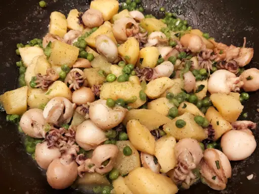 Un gustoso piatto di seppie e patate, con piselli verdi sparsi, condito con erbe aromatiche.