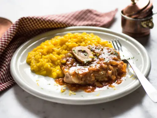 Un succulento ossobuco alla milanese, con il suo midollo invitante, adagiato su un letto di risotto giallo zafferano.