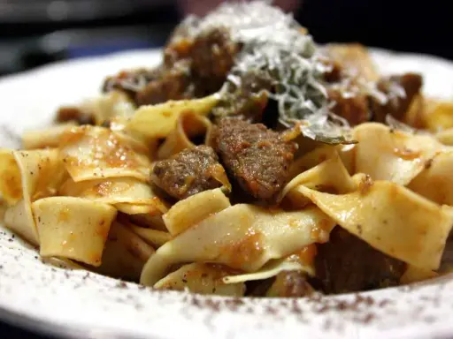 Pappardelle al cinghiale, un piatto ricco e saporito con pasta fresca e ragù di cinghiale, spolverato di parmigiano.