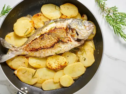Orata in padella con patate e rosmarino, un piatto succulento e profumato, pronto per essere gustato.