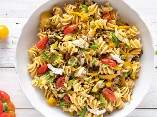Un piatto invitante di pasta fredda saporita con fusilli, pomodorini, zucchine, peperoni gialli e mozzarella.