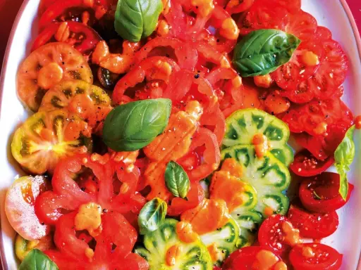 Un'insalata di pomodori colorati, affettati e conditi con erbe aromatiche fresche.