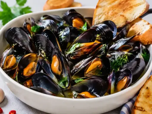 Soute di cozze fumante in una ciotola bianca, guarnita con prezzemolo fresco e accompagnata da fette di pane tostato.