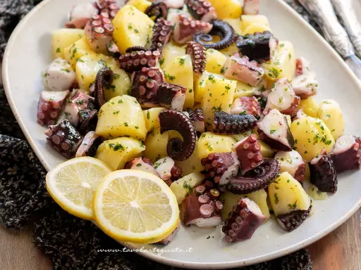 Un invitante polpo con patate, condito con prezzemolo e servito con spicchi di limone.