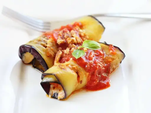 Deliziosi involtini di melanzane ripieni, conditi con sugo di pomodoro e basilico fresco, pronti per essere gustati.