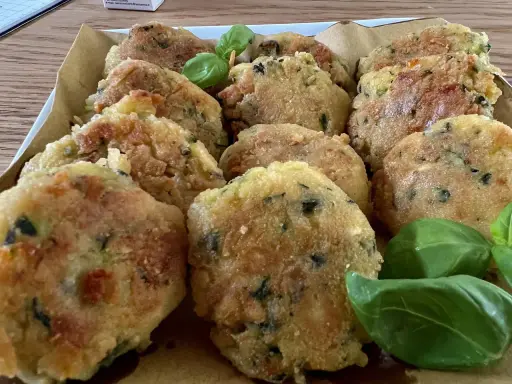 Deliziose polpette di zucchine grattugiate in padella, dorate e croccanti, guarnite con foglie di basilico fresco.