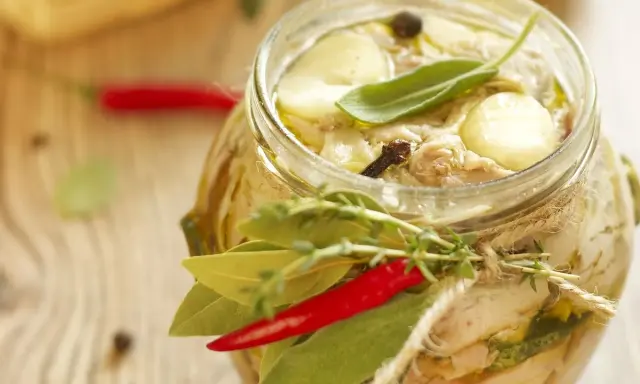 Tonno di coniglio in olio, con erbe aromatiche, peperoncino e spezie, in un barattolo di vetro decorato con spago.