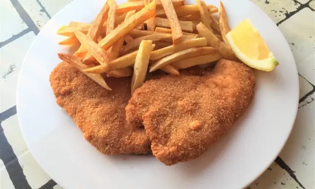 Due cotolette di pollo dorate e croccanti, accompagnate da patatine fritte e uno spicchio di limone.
