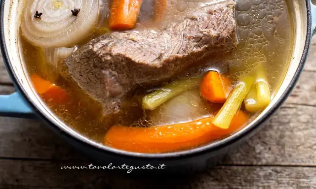 Un pezzo di carne succulenta cuoce lentamente in un brodo di carne ricco, con carote, sedano e cipolla.