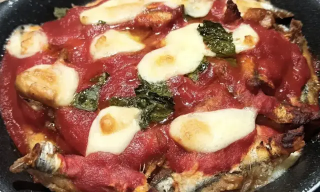 Parmigiana di alici in teglia, con pomodoro, mozzarella filante e basilico. Un piatto saporito e invitante.