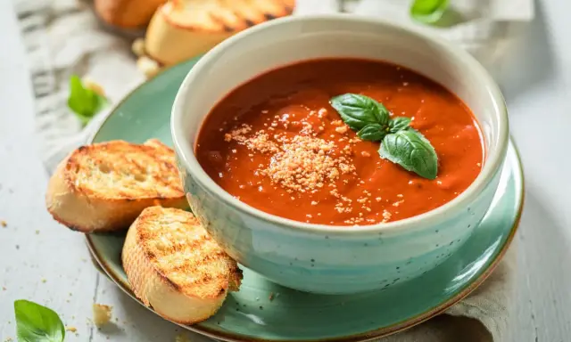 Una ciotola di cremosa zuppa di pomodoro, guarnita con basilico fresco e parmigiano, servita con crostini tostati.