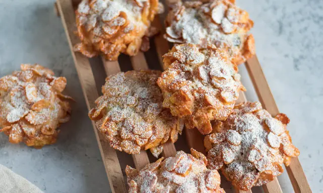Deliziose rose del deserto, dolcetti croccanti ricoperti di fiocchi di mais e spolverati di zucchero a velo, su un tagliere di legno.