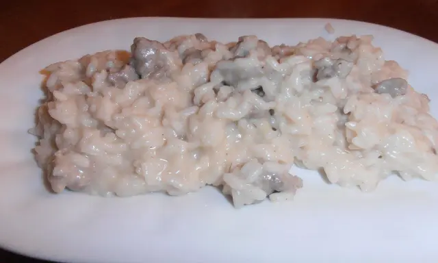 Un cremoso risotto con salsiccia, servito su un piatto bianco.