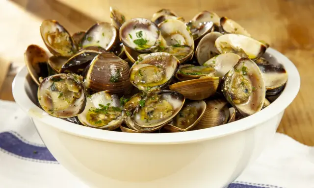 Un invitante sautè di vongole, condito con prezzemolo fresco e olio d'oliva, servito in una ciotola bianca su un tavolo di legno.