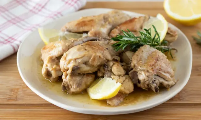 Succulento pollo al limone, dorato e profumato, servito con spicchi di limone fresco e rosmarino su un piatto bianco.