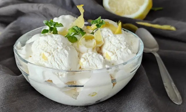 Coppa di cremoso gelato al limone, guarnita con scorzette e foglioline di menta. Un limone fresco sullo sfondo.