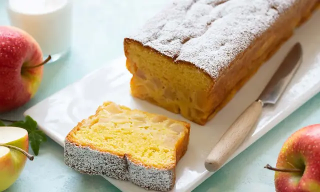 Un delizioso plumcake alle mele, cosparso di zucchero a velo, con una fetta tagliata e mele rosse fresche accanto.