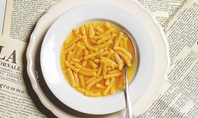 Passatelli in brodo, un classico della ricetta italiana, serviti in un piatto bianco su vecchie pagine di giornale.