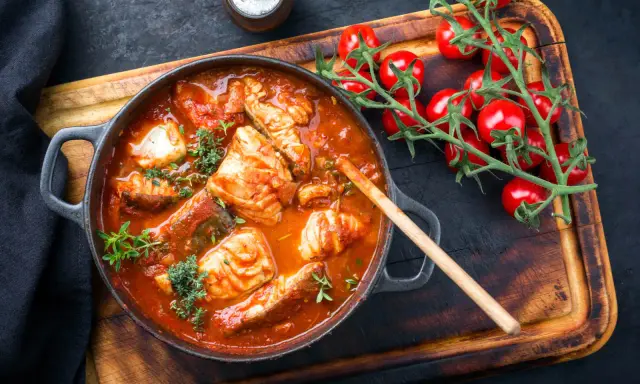 Un invitante guazzetto di pesce in umido, con pomodorini freschi e erbe aromatiche, pronto per essere gustato.