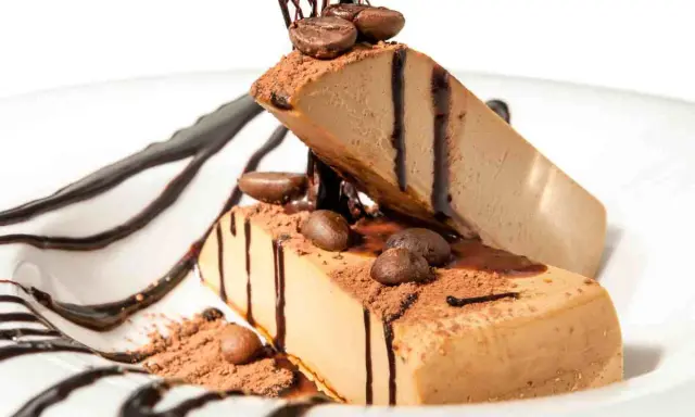 Due fette di semifreddo al caffè, decorate con cacao, chicchi di caffè e salsa al cioccolato, su un piatto bianco.