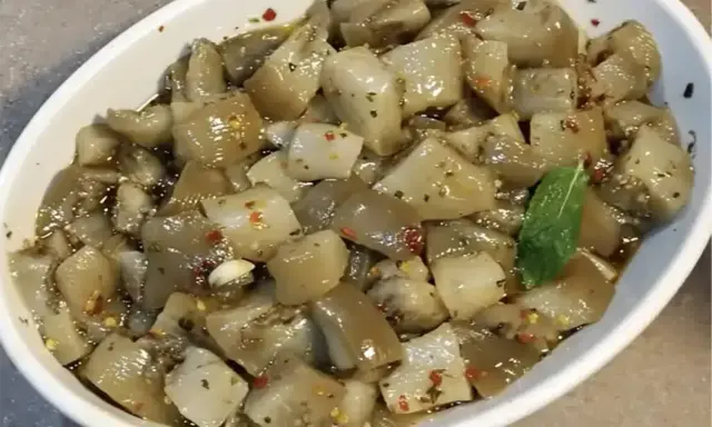 Un invitante piatto di insalata di melanzane, condita con olio, aglio e peperoncino, guarnita con una fogliolina di menta.