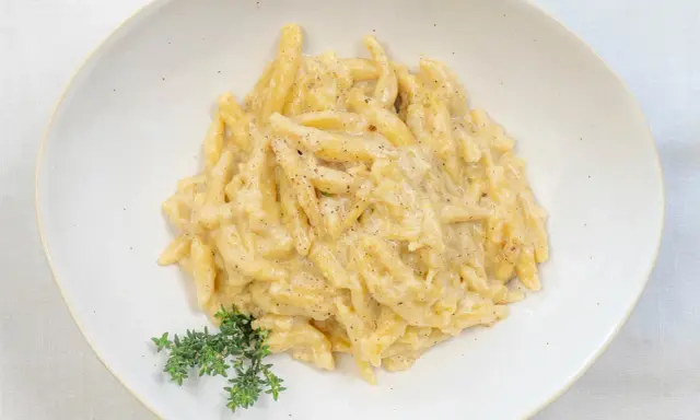 Ravioles val Varaita, pasta fresca condita con una cremosa salsa al formaggio e pepe nero, guarnita con timo fresco.