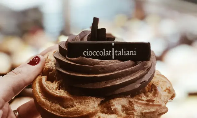 Una mano con smalto rosso tiene un delizioso dolce al cioccolato, decorato con la scritta "cioccolatitaliani".